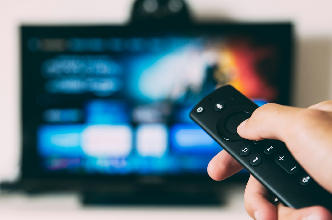 Hand holding a remote control in front of a television